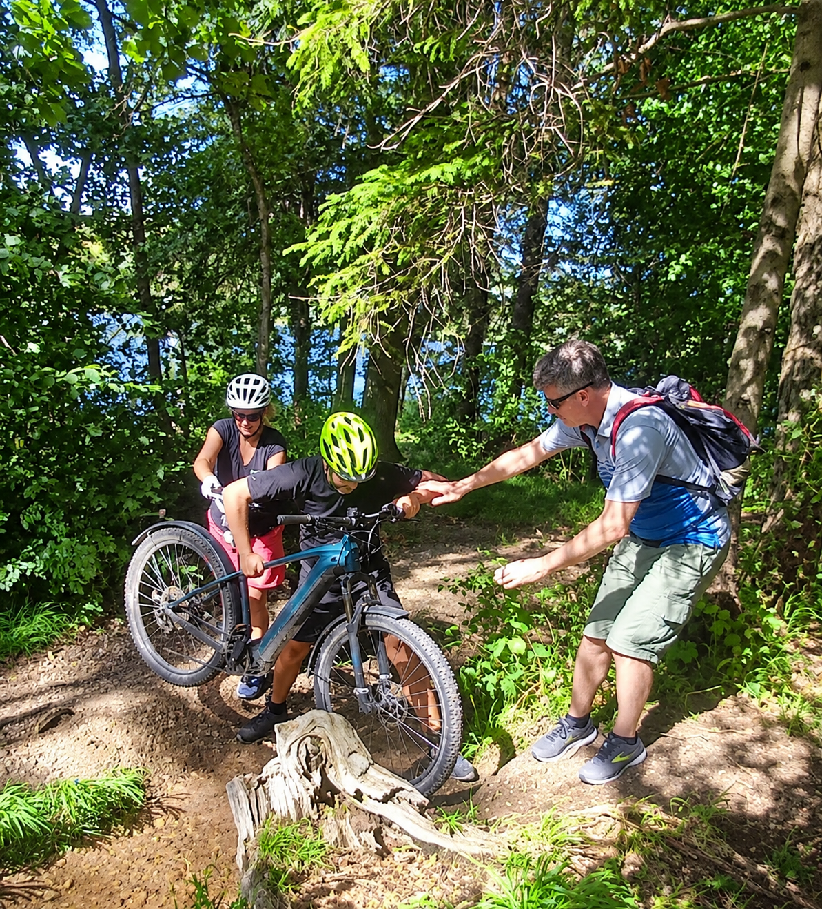 Drei Personen helfen beim Retreat, ein Fahrrad über einen Bach im Wald zu tragen.