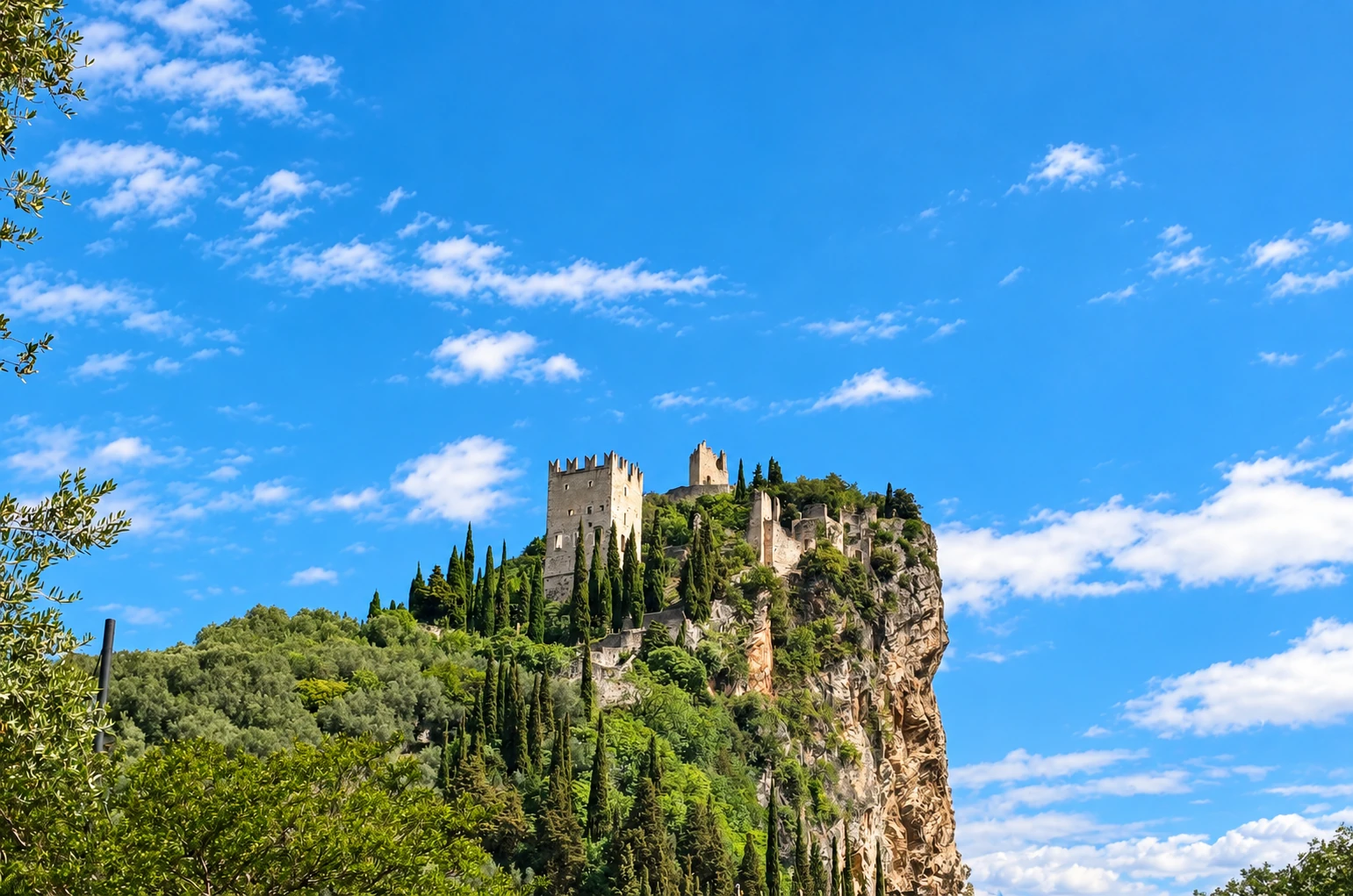Burg auf einem bewachsenen Felsen unter blauem Himmel mit weißen Wolken.